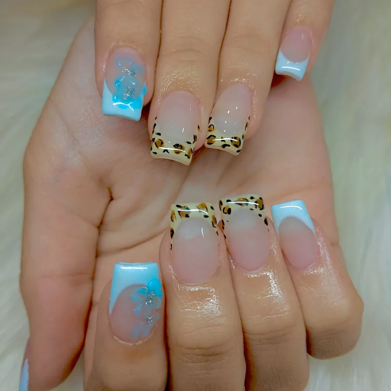 Soft French tips with hand painted blue flowers and leopard accents, nail art by the Sylvia’s team